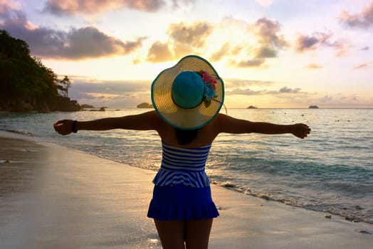 Tourist girl in a swimsuit blue and white striped hat standing on beach with pleasure the beautiful landscape of sky and sea during sunrise, Miang island, Similan National Park, Phang Nga, Thailand