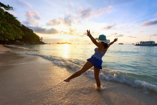 Tourist girl in a swimsuit blue and white striped hat standing on beach with pleasure the beautiful landscape of sky and sea during sunrise, Miang island, Similan National Park, Phang Nga, Thailand