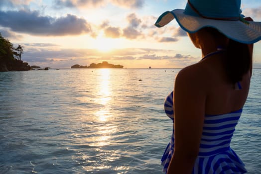 Girl with blue and white striped swimsuit standing watch nature sky and sea during the sunrise on beach of Honeymoon Bay at Koh Miang, Similan Islands National Park, Phang Nga, Thailand