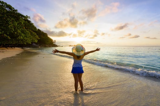 Tourist girl in a swimsuit blue and white striped hat standing on beach with pleasure the beautiful landscape of sky and sea during sunrise, Miang island, Similan National Park, Phang Nga, Thailand