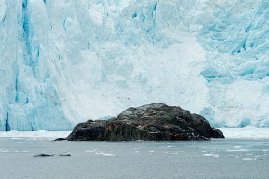 A large rock outcropping sits in front of a calving glacier