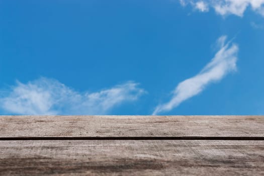 Wooden floor with blue sky and white cloud background