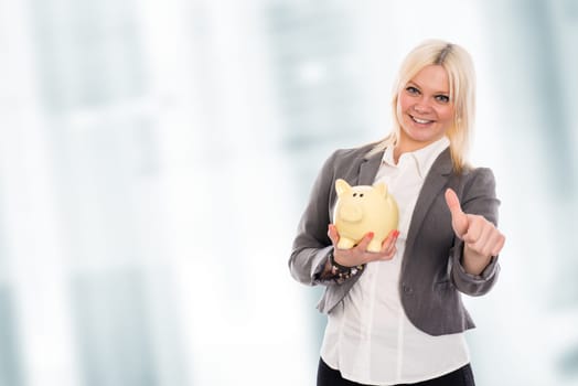 smiling blond young business woman with piggy bank and thumb up