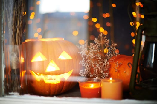 Halloween pumpkin and burning candles in window