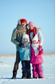 Happy family of four in winterwear looking at camera outdoors