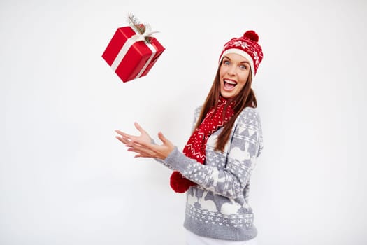 Crazy girl in cap, sweater and scarf throwing xmas present