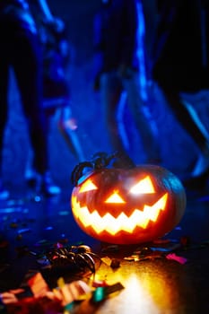 Jack-o-lantern and spiders in darkness on background of dancing people