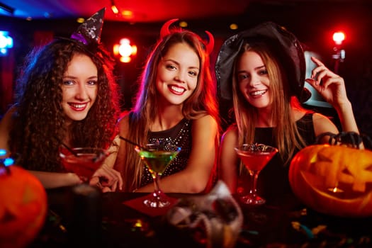 Happy young witches drinking cocktails at bar counter