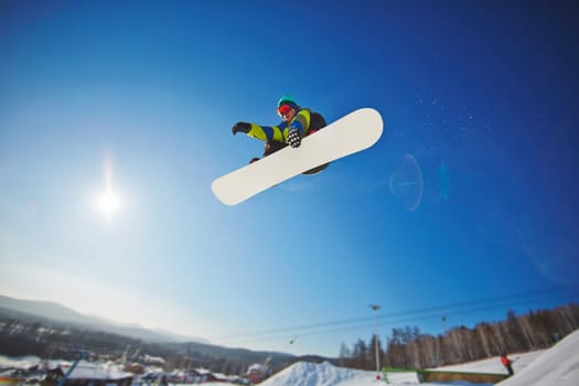 Active young man snowboarding against blue sky