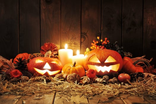 illuminated Halloween pumpkins,candles,nuts,corn cobs and apple on straw in front of old weathered wooden boards in candlelight