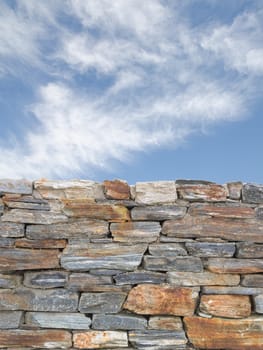 Vertical background with rough stone texture masonry wall and blue cloudy sky