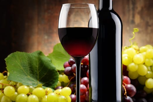 Composition with glass, bottle of red wine and fresh grapes.