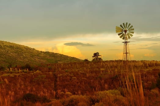 Country life landscape with beautiful prairie fields and old wind mill over sunset sky in the background.