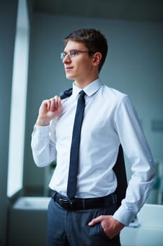Young elegant businessman standing by window in office