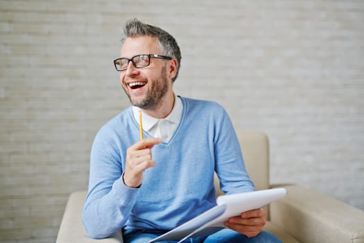 Happy psychiatrist with pencil and clipboard sitting in armchair