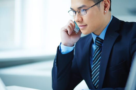 Young Asian businessman in eyeglasses speaking on the phone