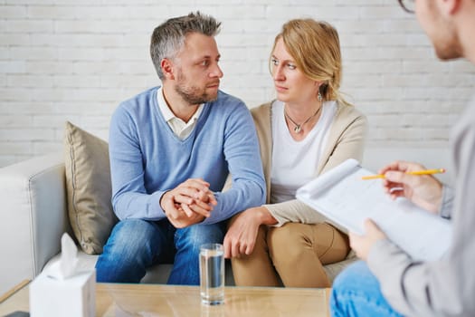 Sad couple sitting on sofa in front of psychologist
