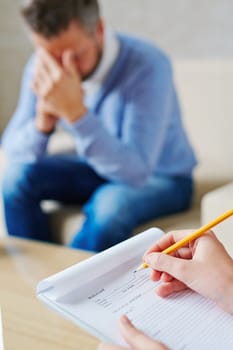 Hands of psychiatrist filling in medical document in front of stressed patient