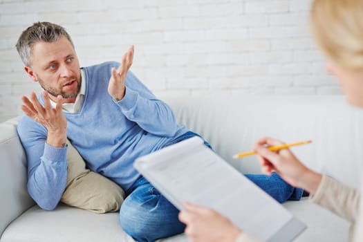 Confused man on sofa telling his psychologist what happened