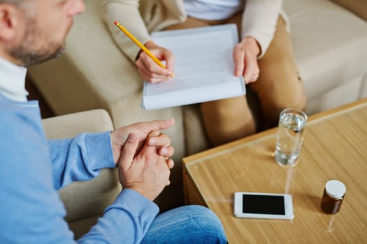Male sitting in armchair while psychiatrist making notes in medical document