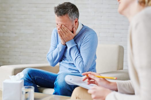 Stressed man with his hands on face sitting by psychologist