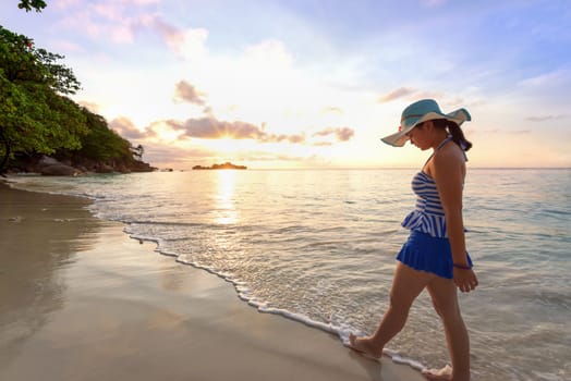 Girl in blue swimsuit walking on beach with happy and beautiful sky above the sea during sunrise at Honeymoon Bay, Koh Miang Islands, Similan National Park, Phang Nga, Thailand