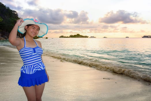 Woman in swimsuit standing poses on beach with happy and beautiful sky above the sea during sunrise at Honeymoon Bay, Koh Miang Island, Similan National Park, Phang Nga, Thailand