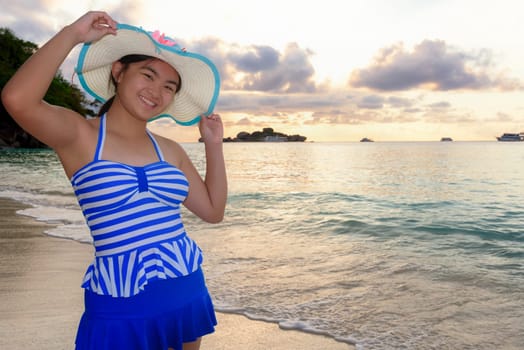 Woman in swimsuit standing poses on beach with happy and beautiful sky above the sea during sunrise at Honeymoon Bay, Koh Miang Island, Similan National Park, Phang Nga, Thailand