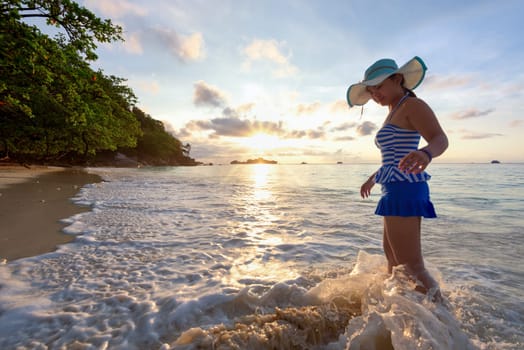 Girl in a swimsuit standing sand and water play with happiness during sunrise on the beach of Honeymoon Bay at Koh Miang, Similan Islands National Park, Phang Nga, Thailand