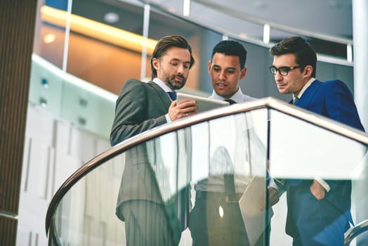 Serious businessmen in formalwear using touchpad at meeting