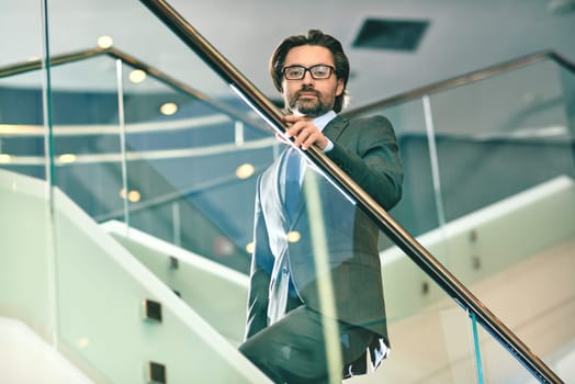 Mature businessman looking at camera while going upstairs
