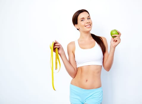Fit young woman with green apple and measuring tape looking at camera