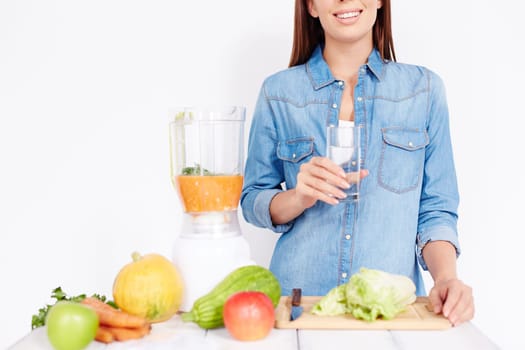 Young female with glass of water cooking breakfast from vegetables