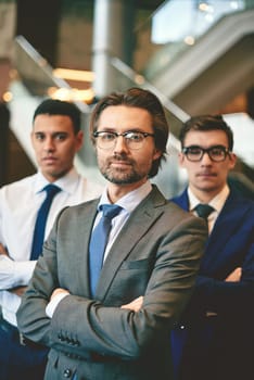 Mature businessman looking at camera with two colleagues behind