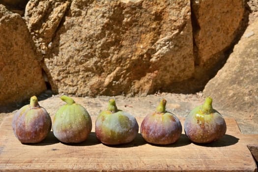 Composition of fig fruits on a wooden board and rocks in the background.