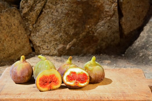 Composition of fig fruits on a wooden board and rocks in the background.