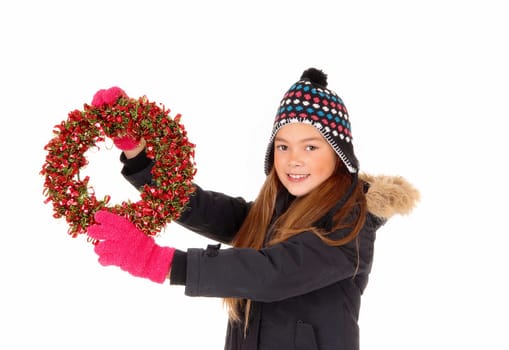 A closeup picture of a young pretty girl holding up a colorful advents.wreath, in a jacket, mittens and hat, isolated on white background..