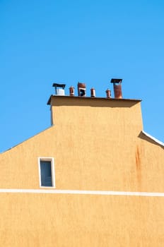 Chimney section of yellow house wall with different chimney caps on blue sky background