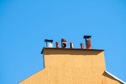 Chimney section of yellow house wall with different chimney caps on blue sky background