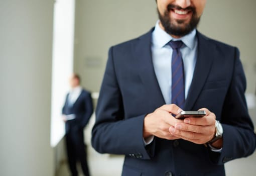 Close-up of young businessman using cellular phone on background of his colleague