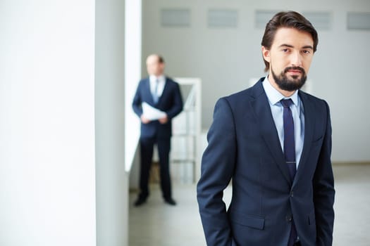 Elegant businessman looking at camera on background of his colleague