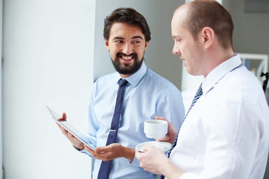 Young businessman with touchpad showing data to his colleague at meeting