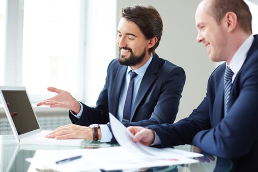 Happy businessman pointing at laptop screen while explaining ideas to his colleague