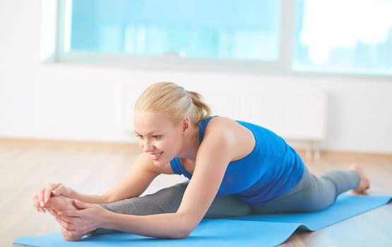 Sportive blonde doing stretching exercise on mat