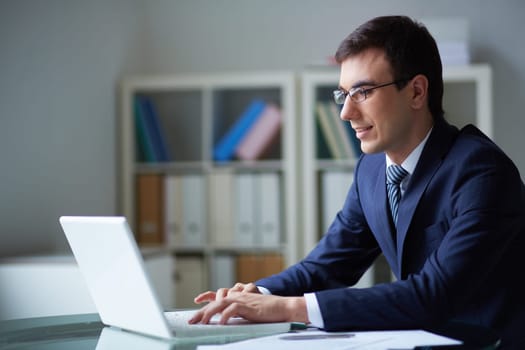 Smiling businessman in suit typing on laptop in office