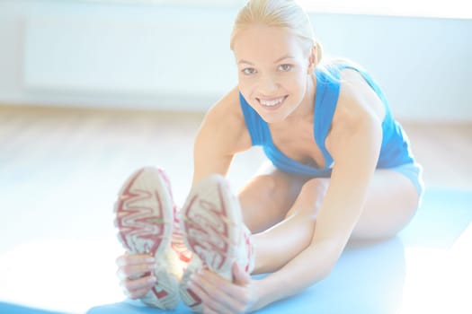 Fit woman doing stretching exercise and looking at camera