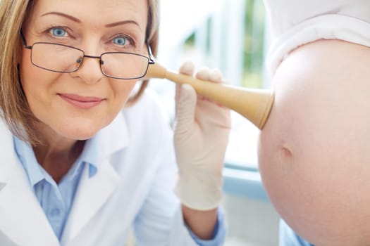 Mature gynecologist examining the heartbeat of baby in female belly