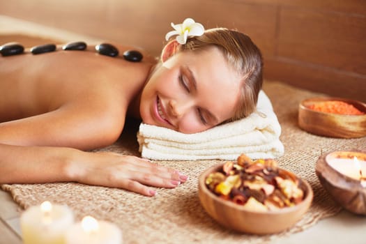 Peaceful woman relaxing in spa salon with her head on folded soft towel and hot stones on her back