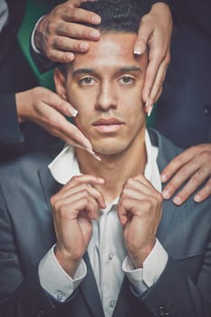 Stylish guy with female and male hands on his head looking at camera