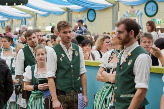 MUNICH, GERMANY – SEPT. 19, 2015: Men and Women Staff in the Spatenbrau Tent with Traditional Costumes Serve Visitors at the Annual Oktoberfest. The Festival runs from September 19th until October 4th 2015 in Munich, Germany.